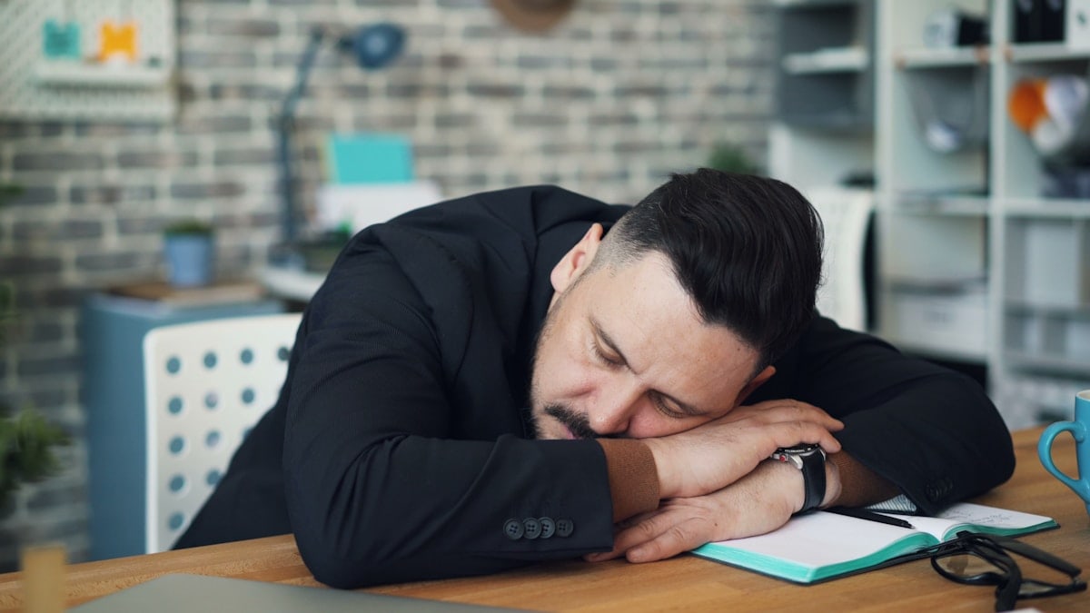 Middle-aged brunet sleeping at work putting head on table sitting at desk alone
