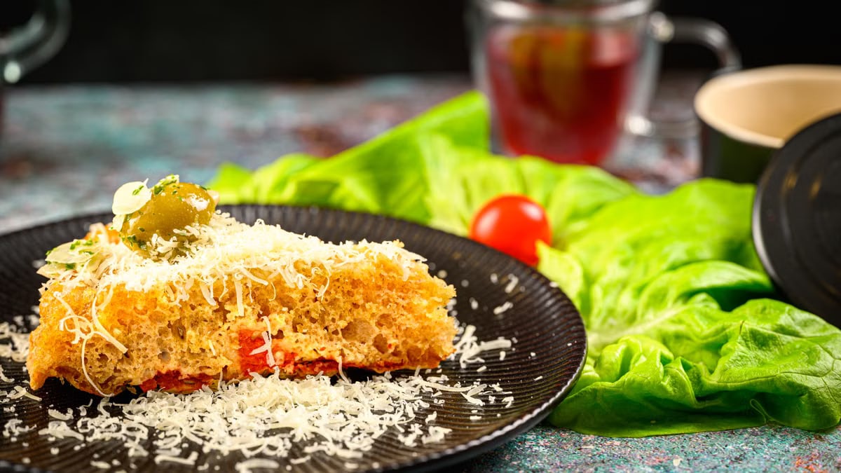 A slice of gourmet bread topped with cheese and olive, surrounded by fresh lettuce and tomato.